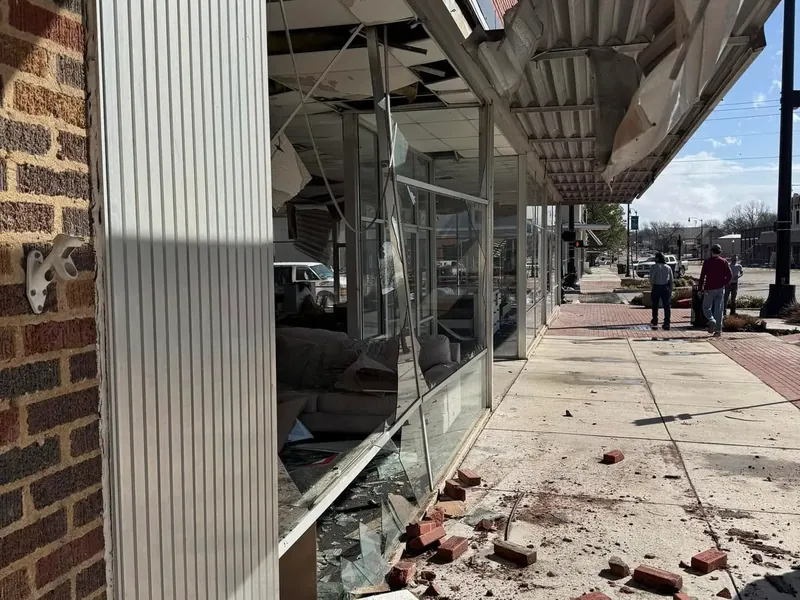 Storefront with shattered windows and fallen bricks on sidewalk, C&A Roofing & Construction