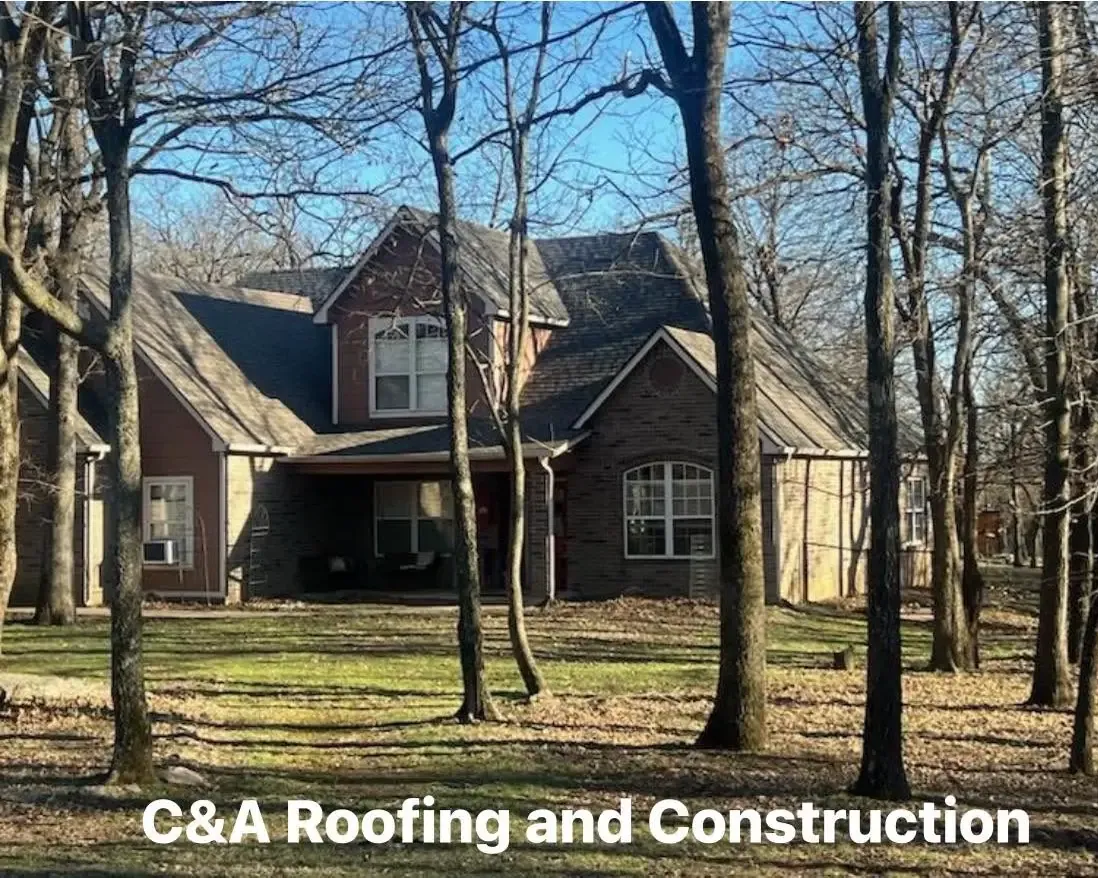 Large brick and stone home among bare trees, C&A Roofing & Construction