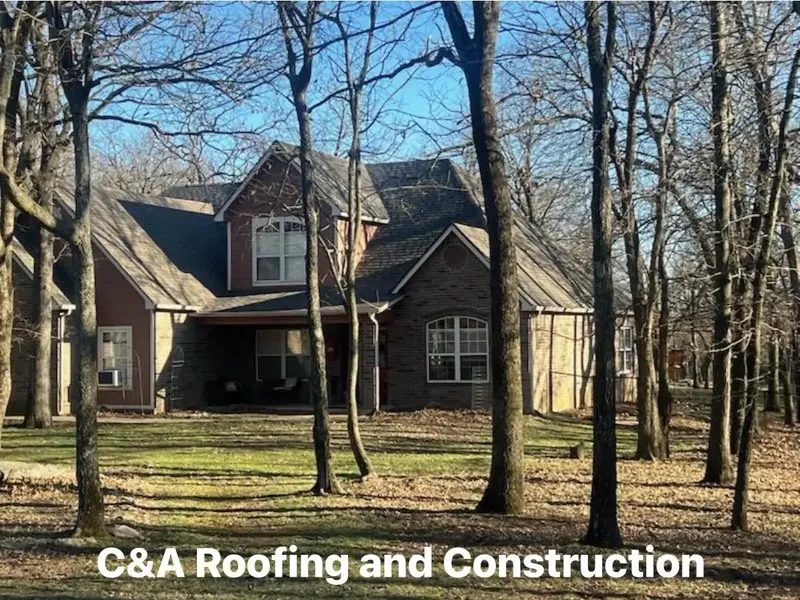 Large brick and stone home among bare trees, C&A Roofing & Construction