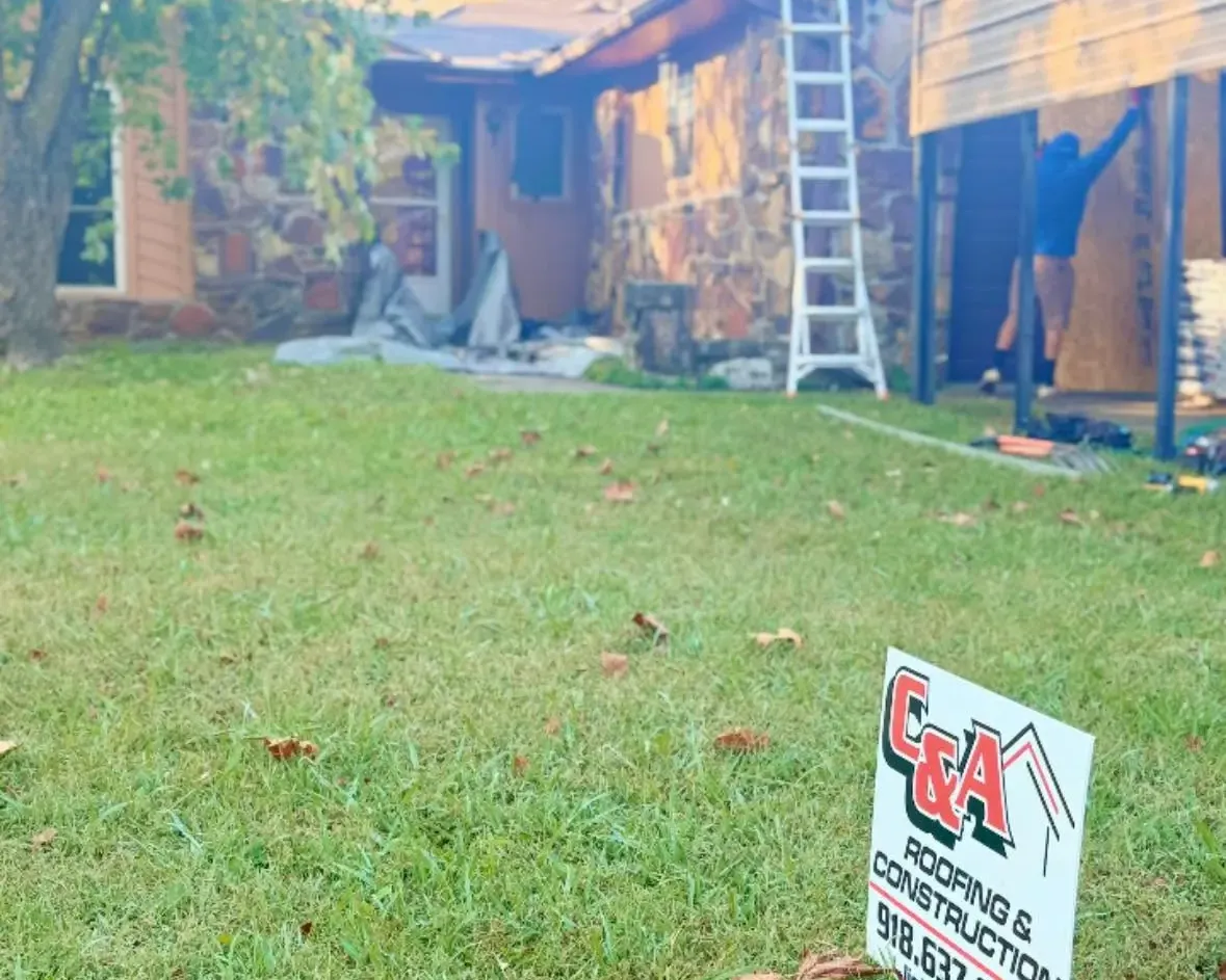 Crew on ladder working on house exterior and carport, yard sign, C&A Roofing & Construction