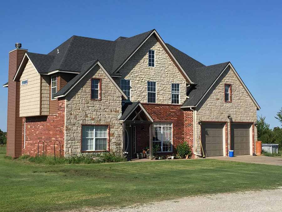 Stunning large stone and brick home featuring multiple architectural elements and professional roofing installation